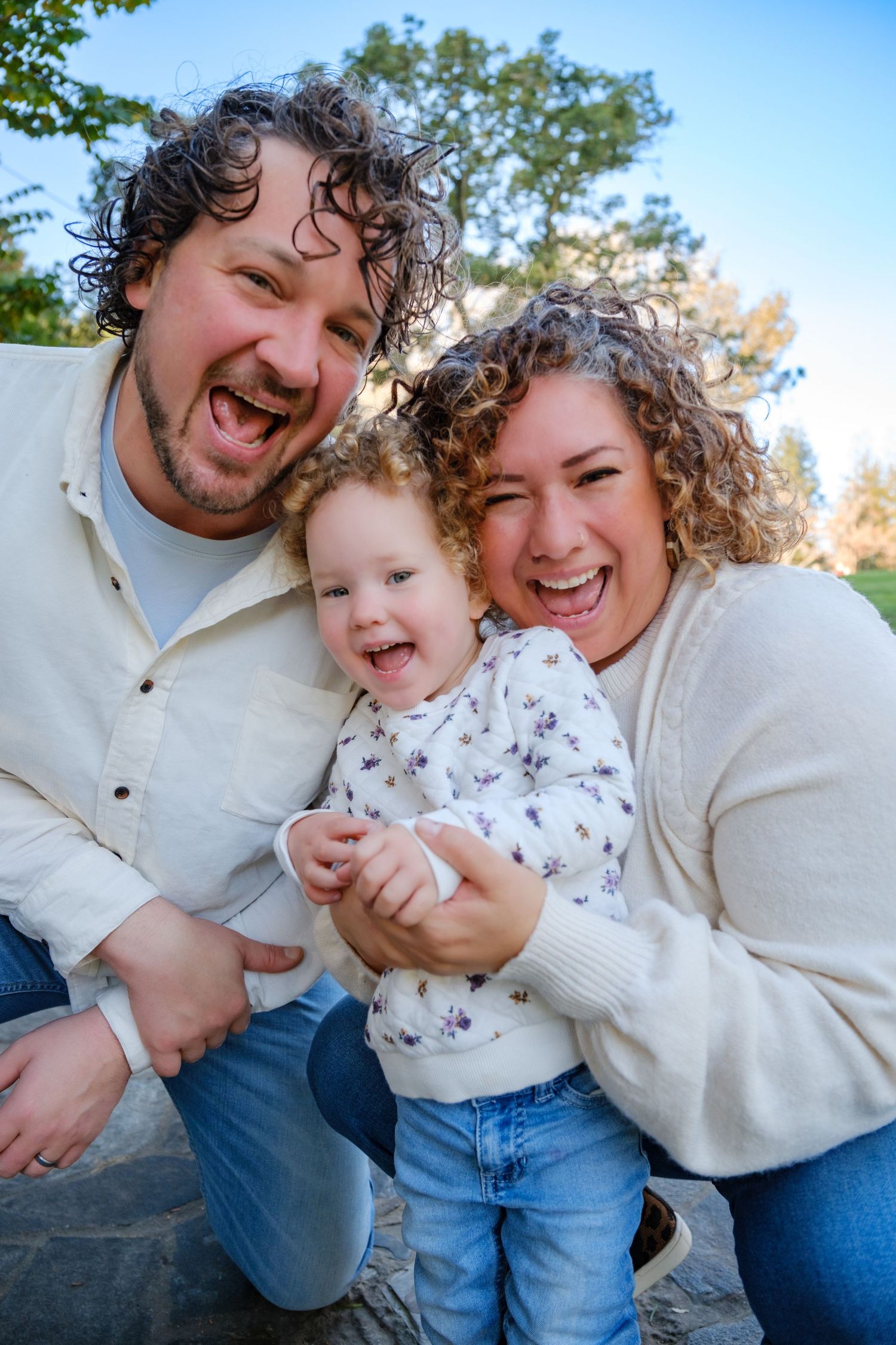A joyful family shares candid moments of laughter and embraces while sitting outdoors in casual attire.