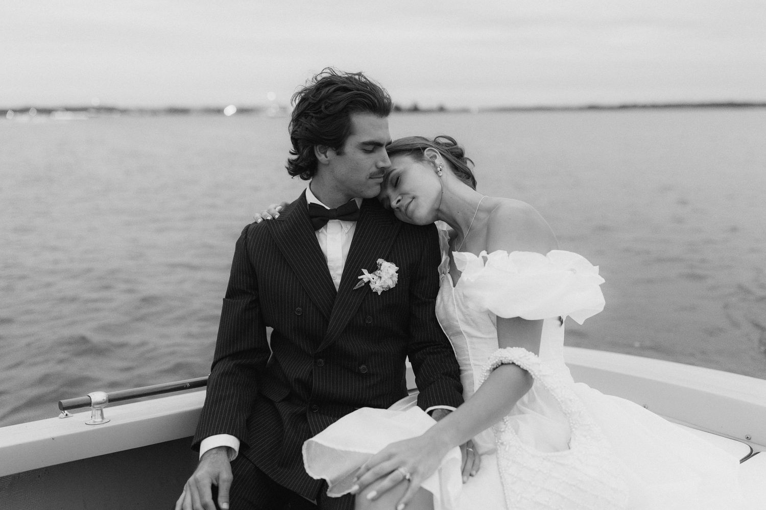 A couple shares an intimate moment on a boat deck during what appears to be a wedding celebration.
