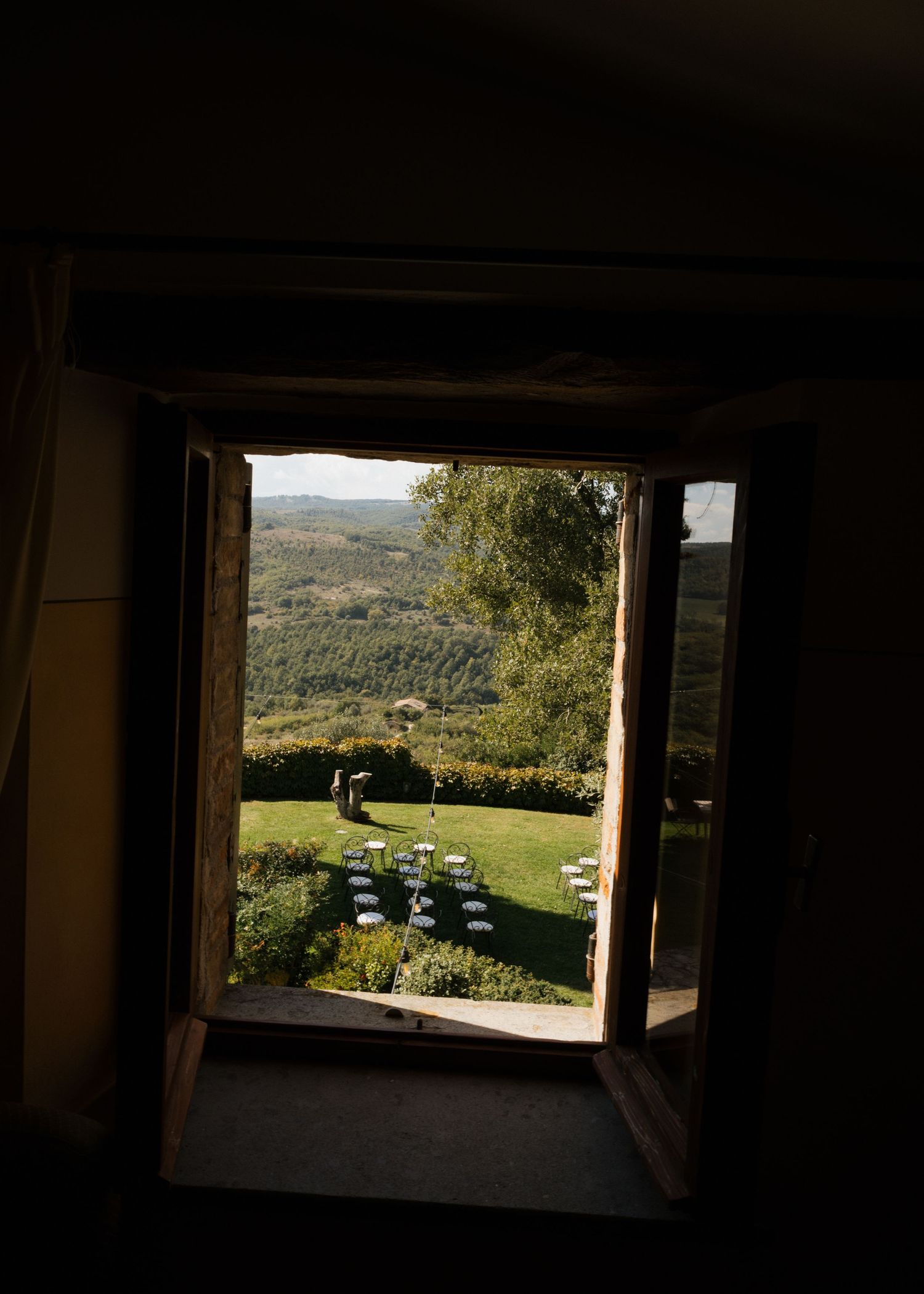 A window frames a scenic view of rolling green hills and countryside with parked cars visible in the distance.