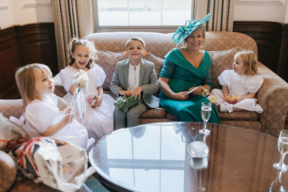 Wedding guests in formal attire sit together on an elegant brown couch during a celebration.