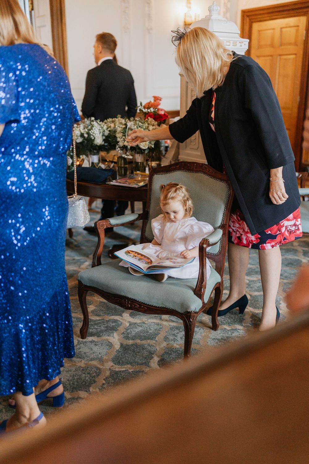 Wedding guests gather in an elegant room with wooden doors and a blue patterned carpet during a formal event.