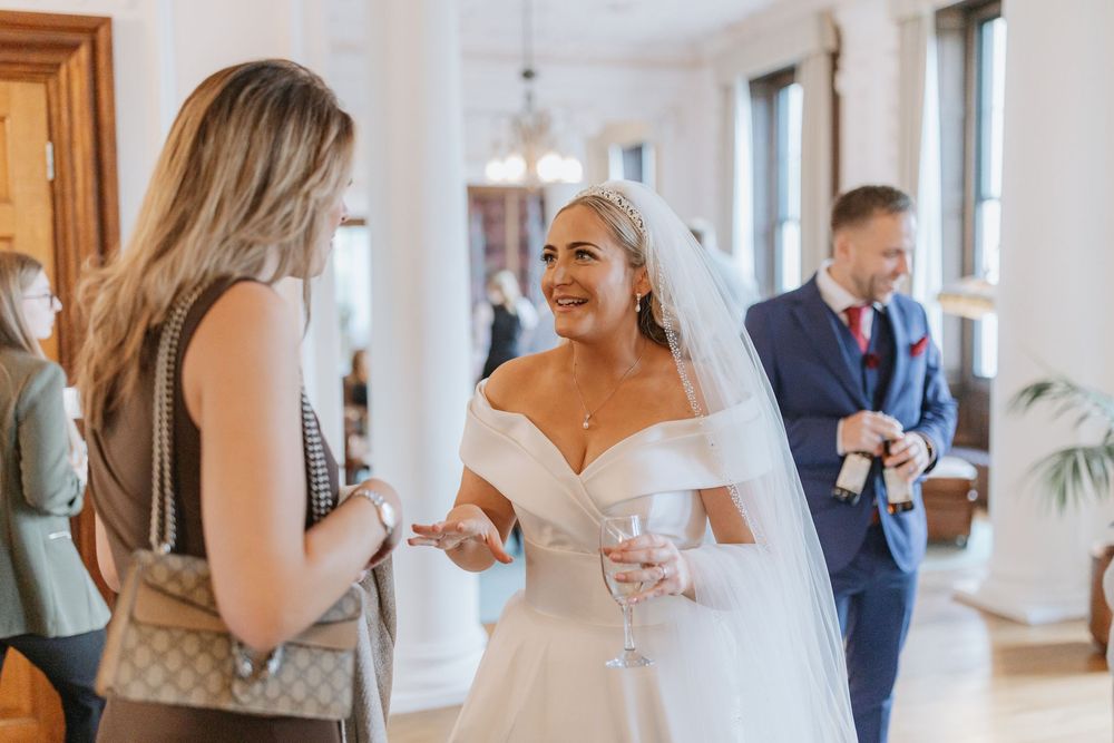 Wedding party members gather in a bright hallway with white walls and wooden trim during pre-ceremony preparations.
