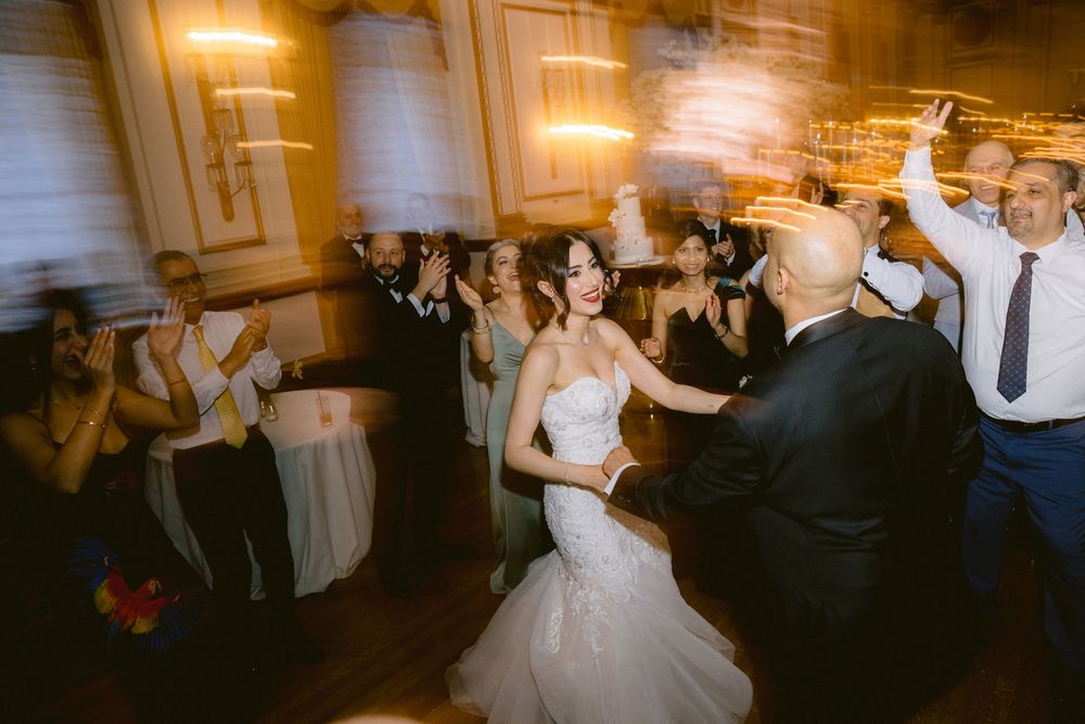 Wedding guests dancing and celebrating on a dimly lit dance floor at an elegant indoor reception venue.