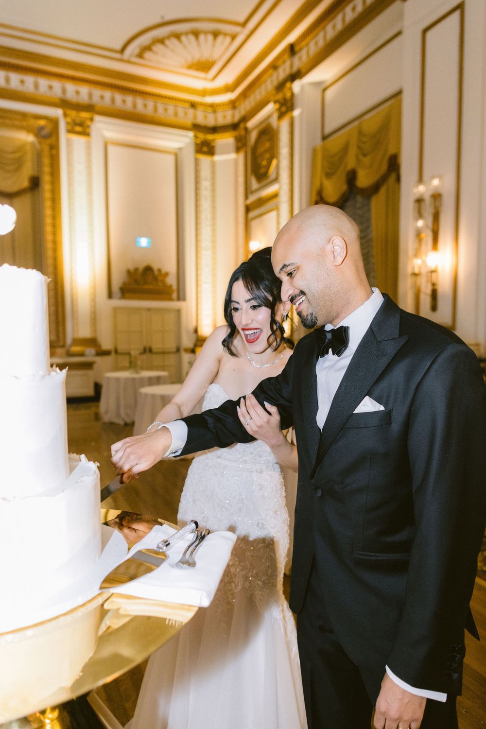 A couple shares a joyful moment during their wedding reception in an elegant gold-trimmed ballroom.
