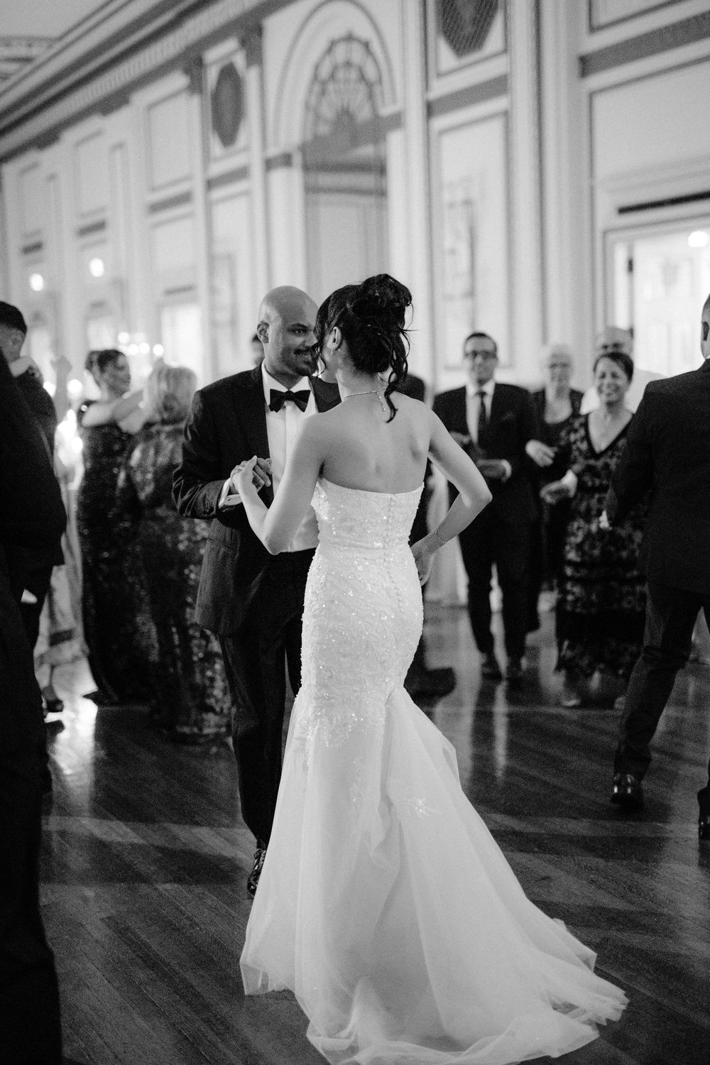 A couple shares an intimate first dance at an elegant wedding reception in a grand ballroom with ornate details.