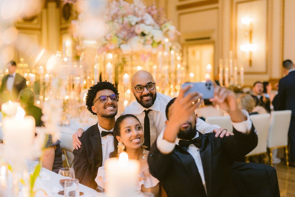 Wedding guests celebrate and take photos during a joyful reception dinner with floral decorations and candlelight.