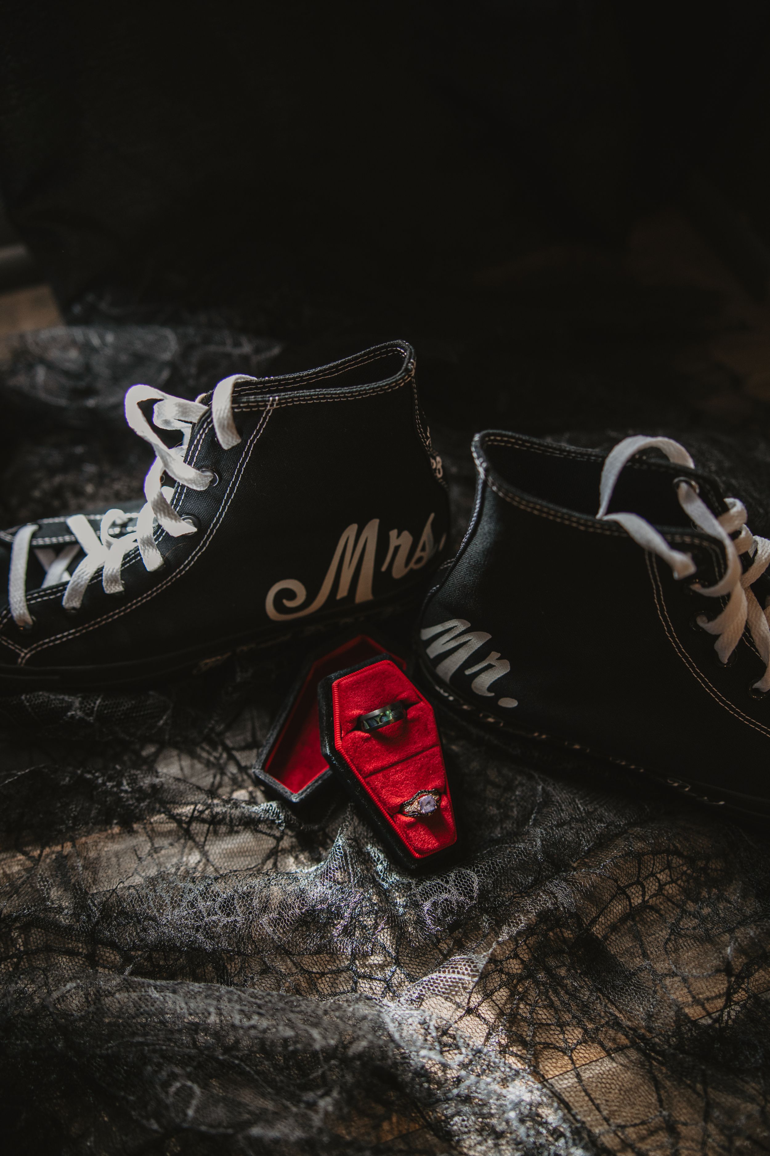 A pair of black and white sneakers with red tags on a textured concrete surface in moody lighting.