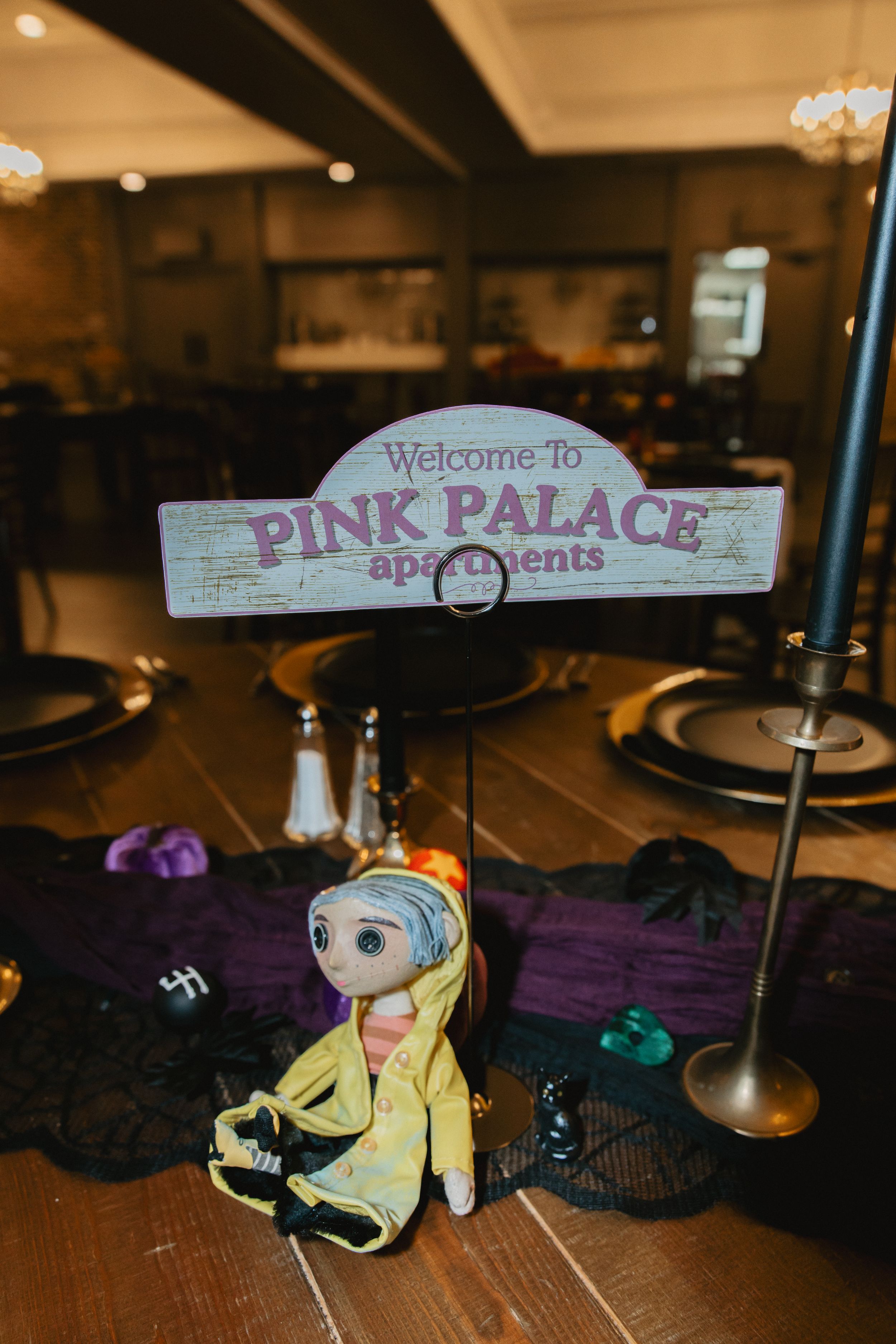 Coraline-themed party decorations featuring a plush doll and purple accents on a dark wooden surface.
