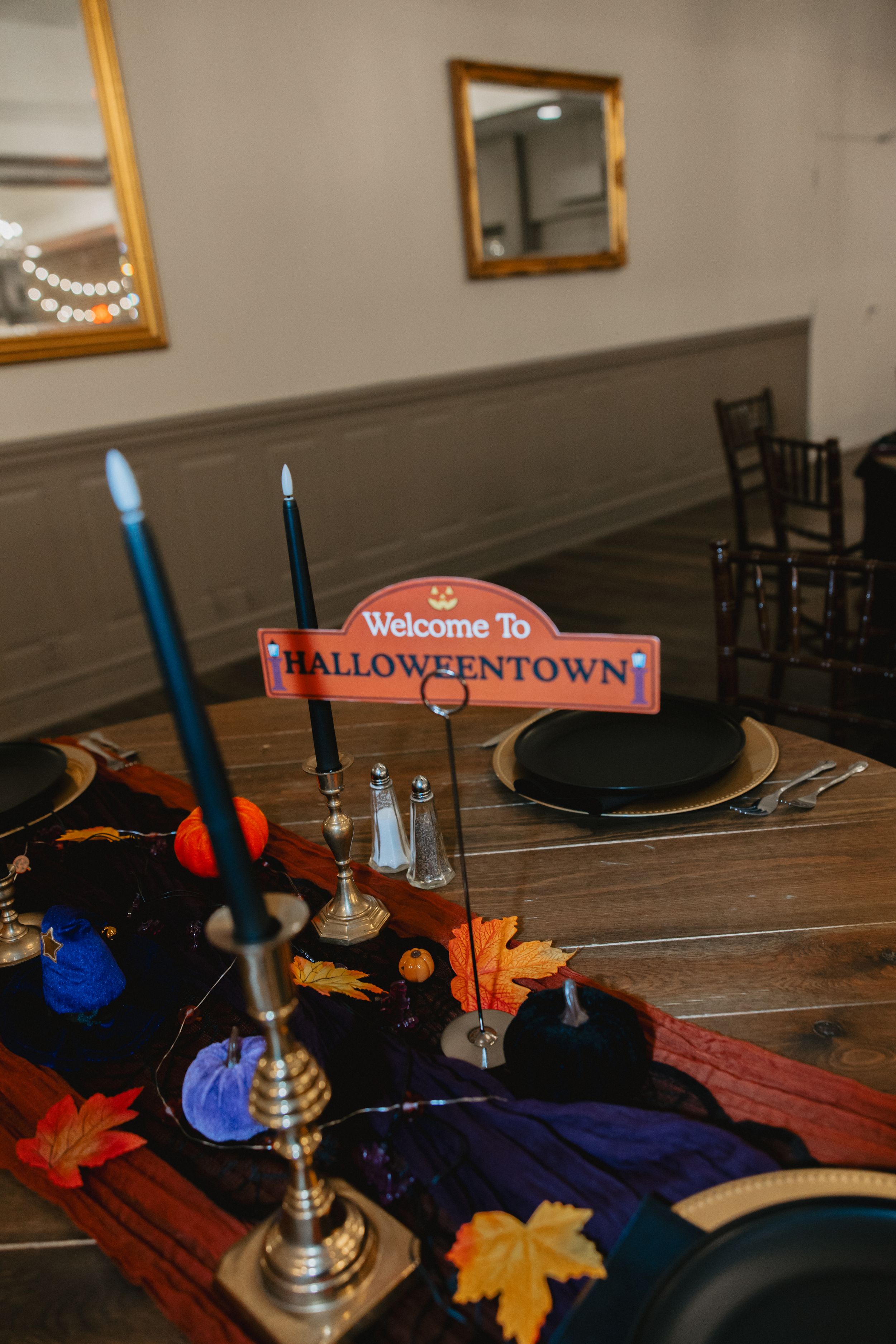 Autumn table setting with black plates, colorful fall leaves, and blue candles in silver candlesticks.