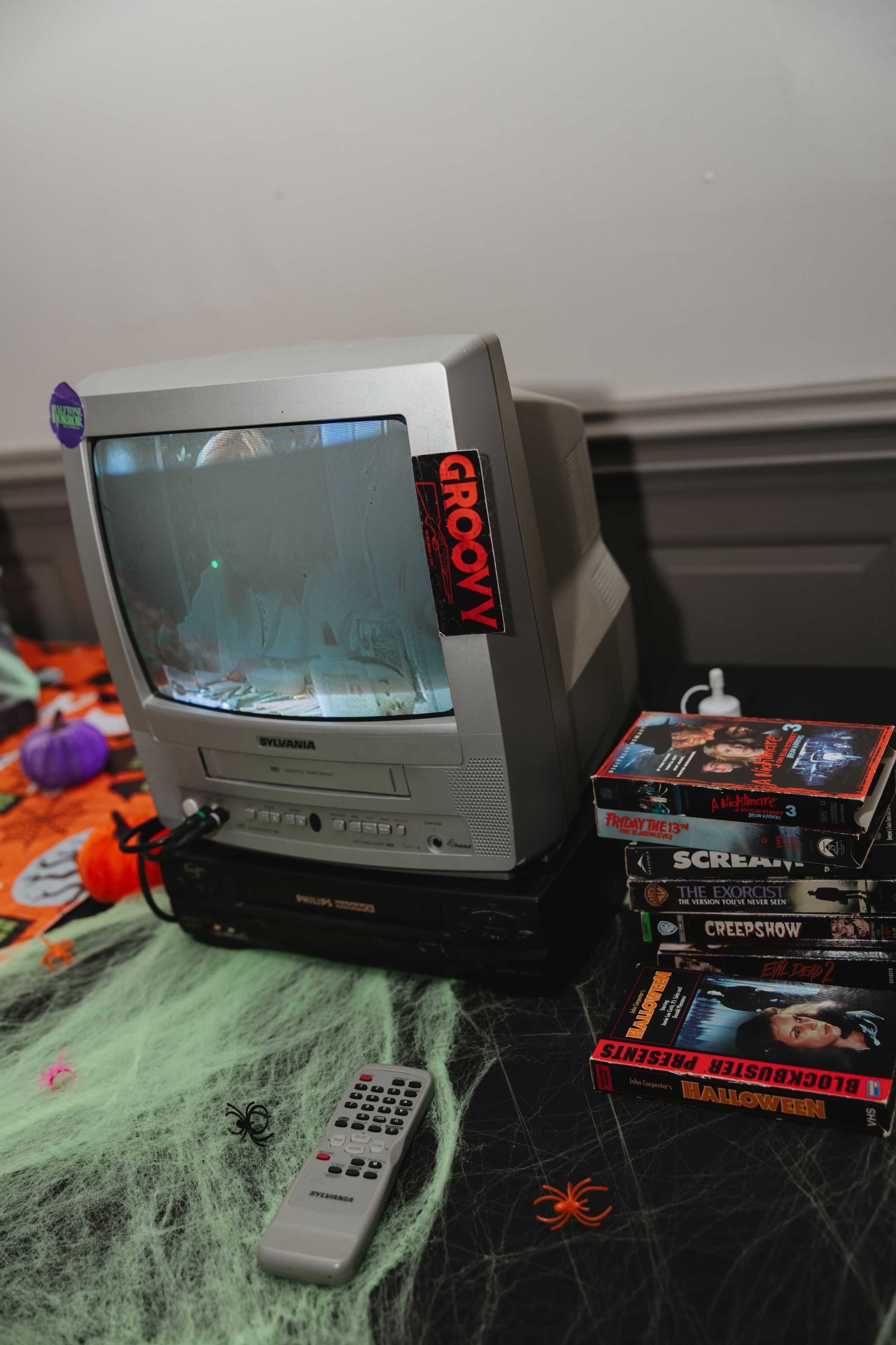 Retro TV setup with spooky Halloween cobweb decorations and horror movies displayed on a green surface.