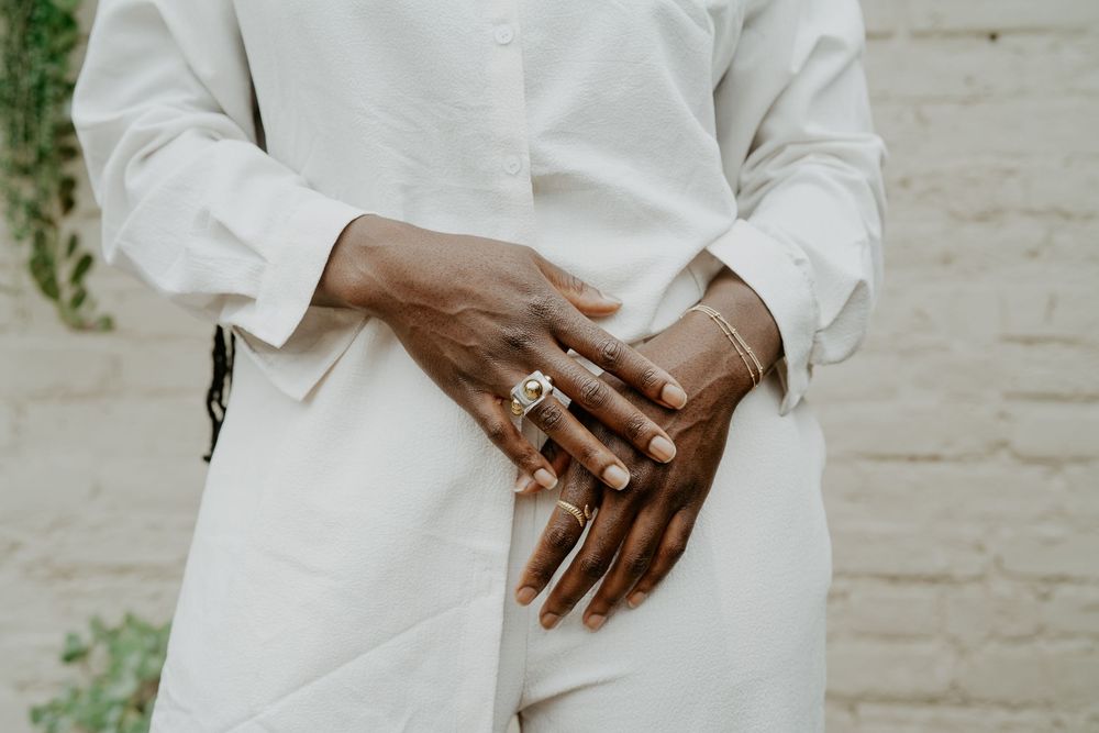 Close-up shot of hands wearing white clothing and jewelry against a light background.