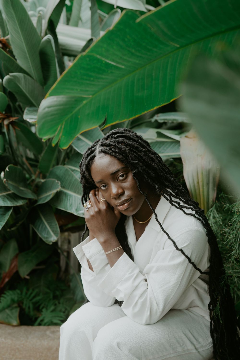 Person in white clothing poses elegantly among tropical foliage and banana leaves.