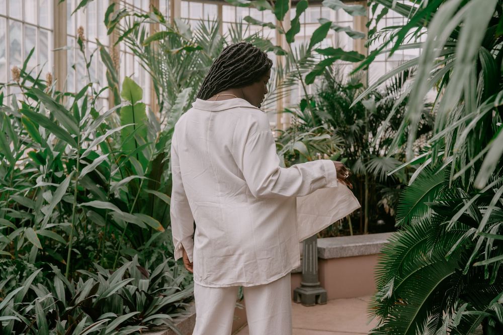 Side view of person in white clothing surrounded by lush greenhouse plants.