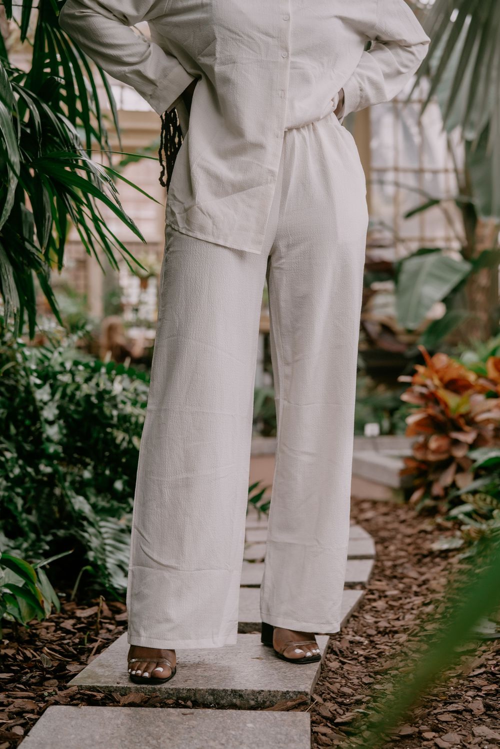 Lower body shot showing white pants and sandals against greenhouse floor.