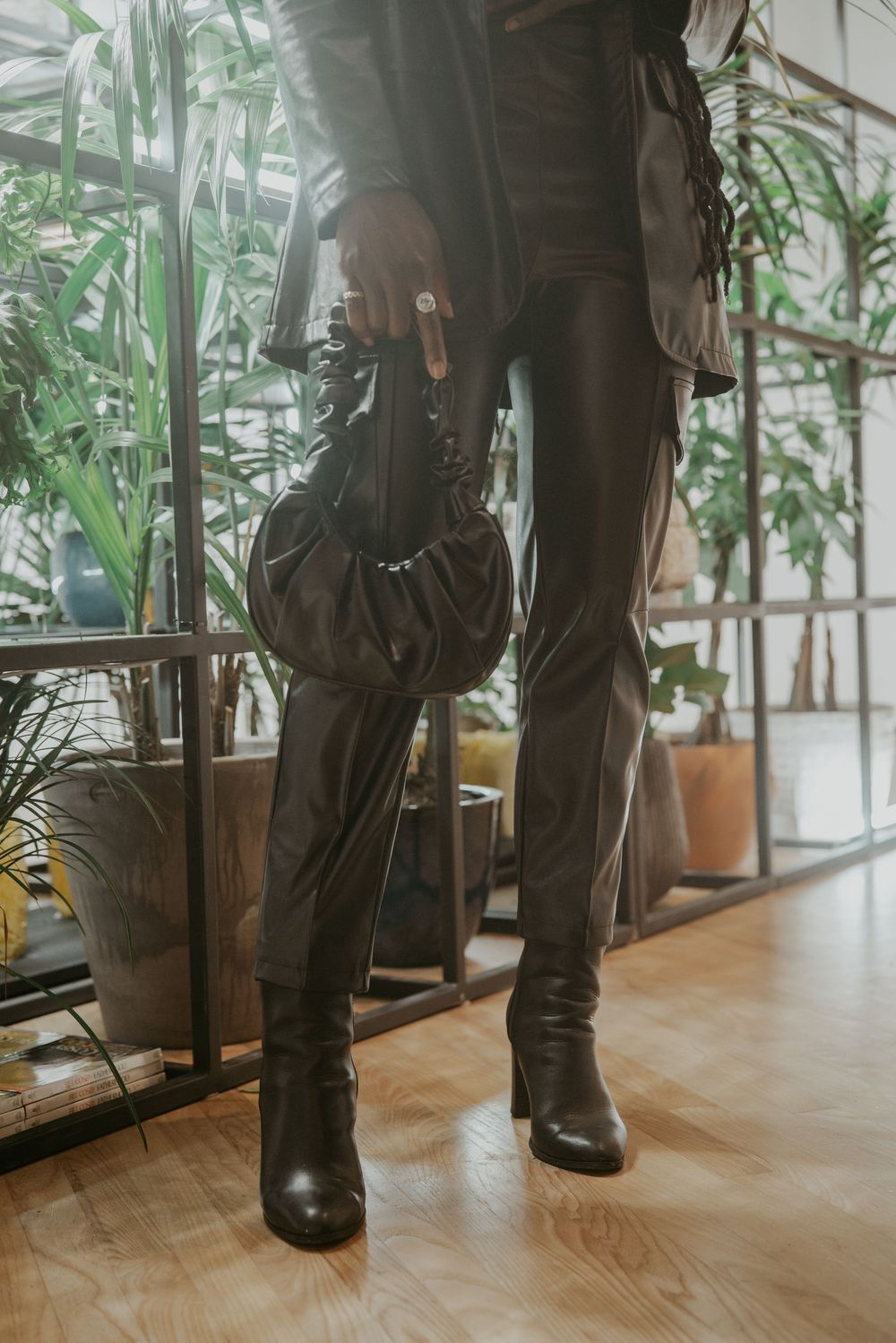 Low angle view of legs wearing dark pants and boots on wooden floor with plants in background.