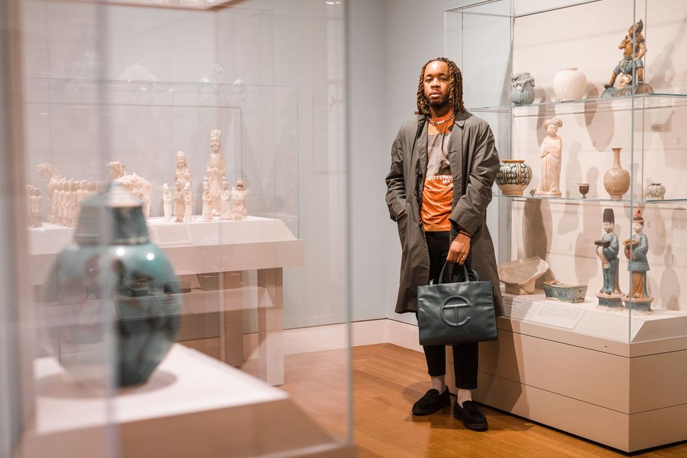 Person in a long coat viewing artifacts displayed in museum glass cases.