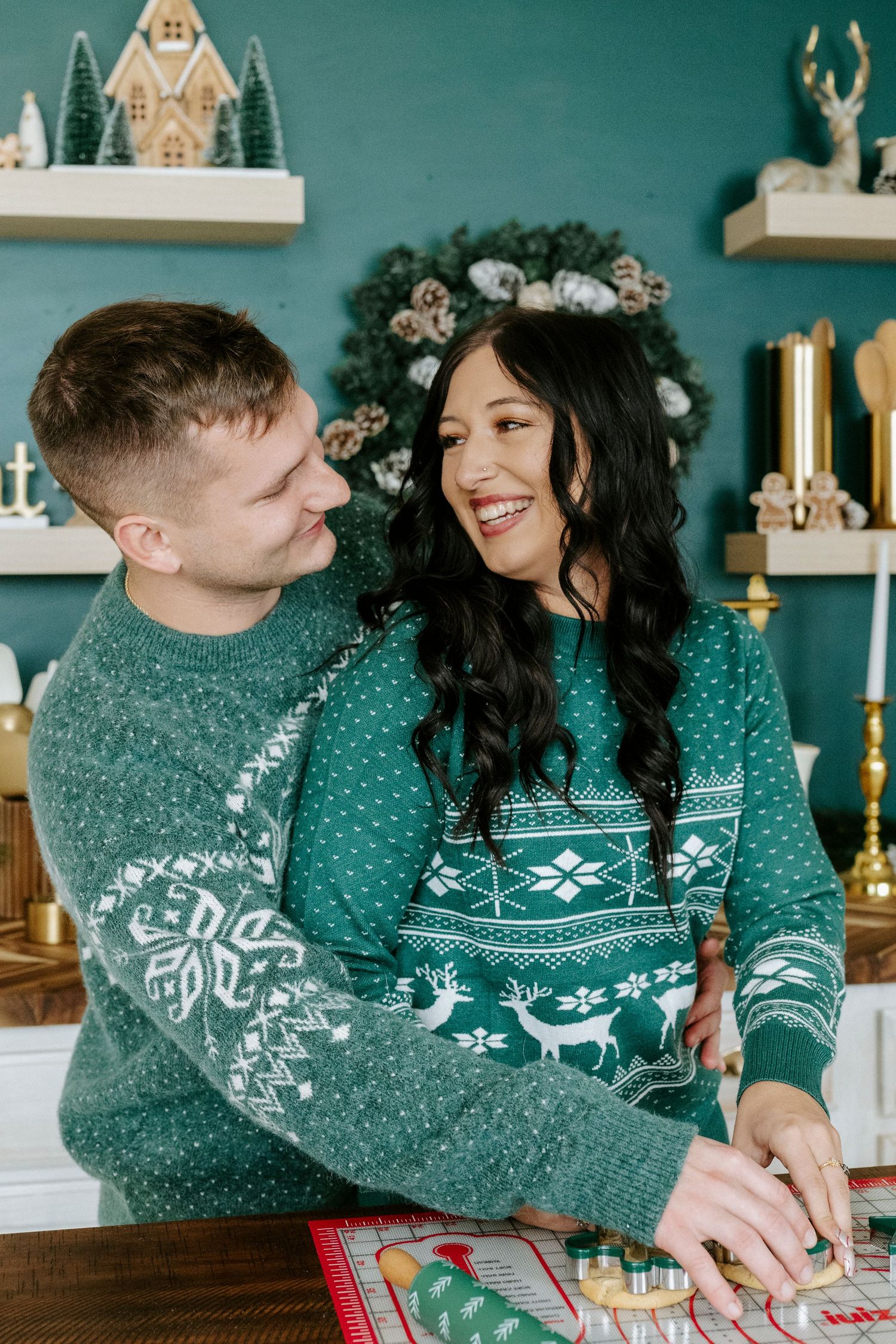 Couple in matching green Nordic sweaters sharing intimate holiday moments while playing board games at home.