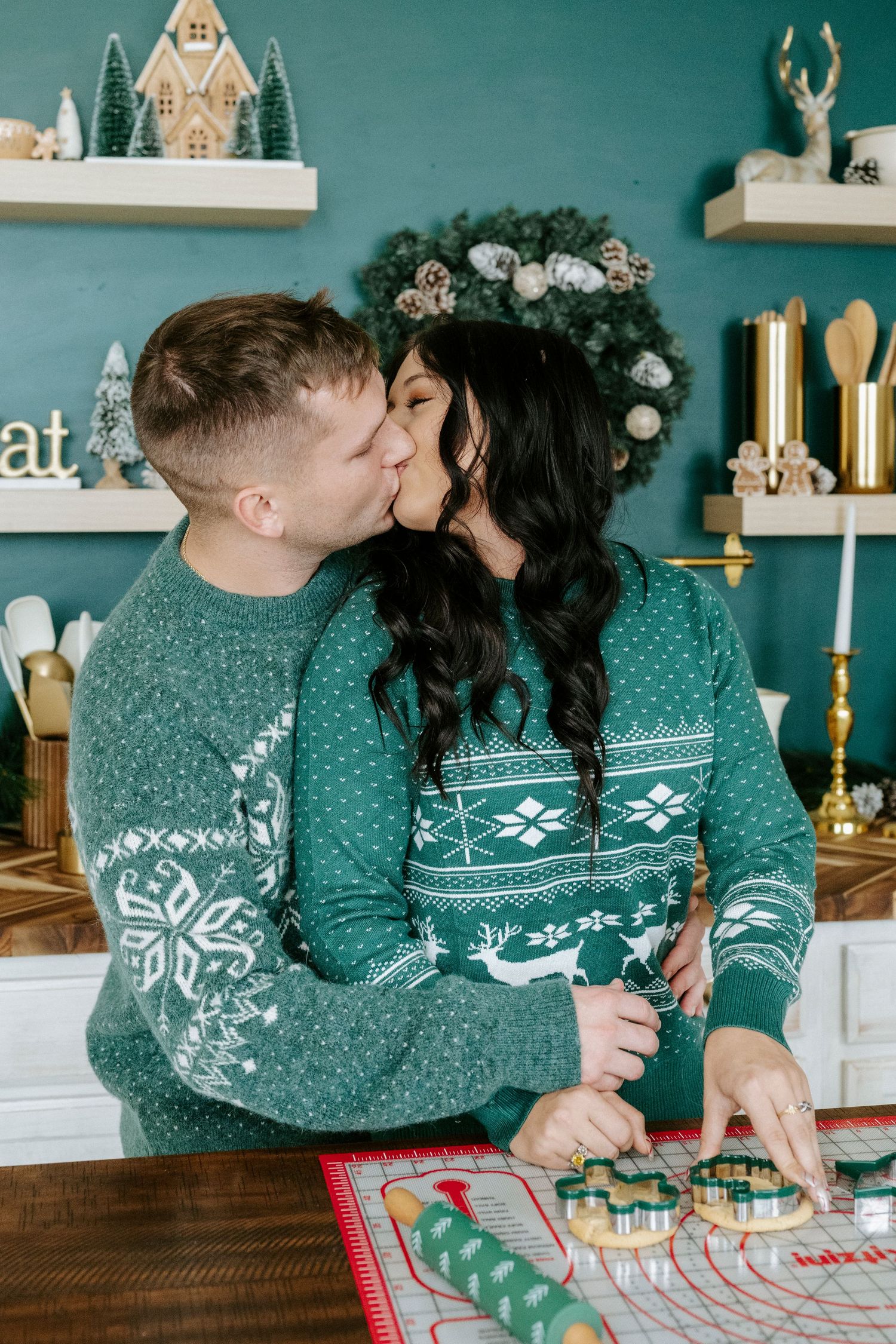 Couple in matching green Nordic sweaters sharing an intimate moment while baking holiday cookies together.