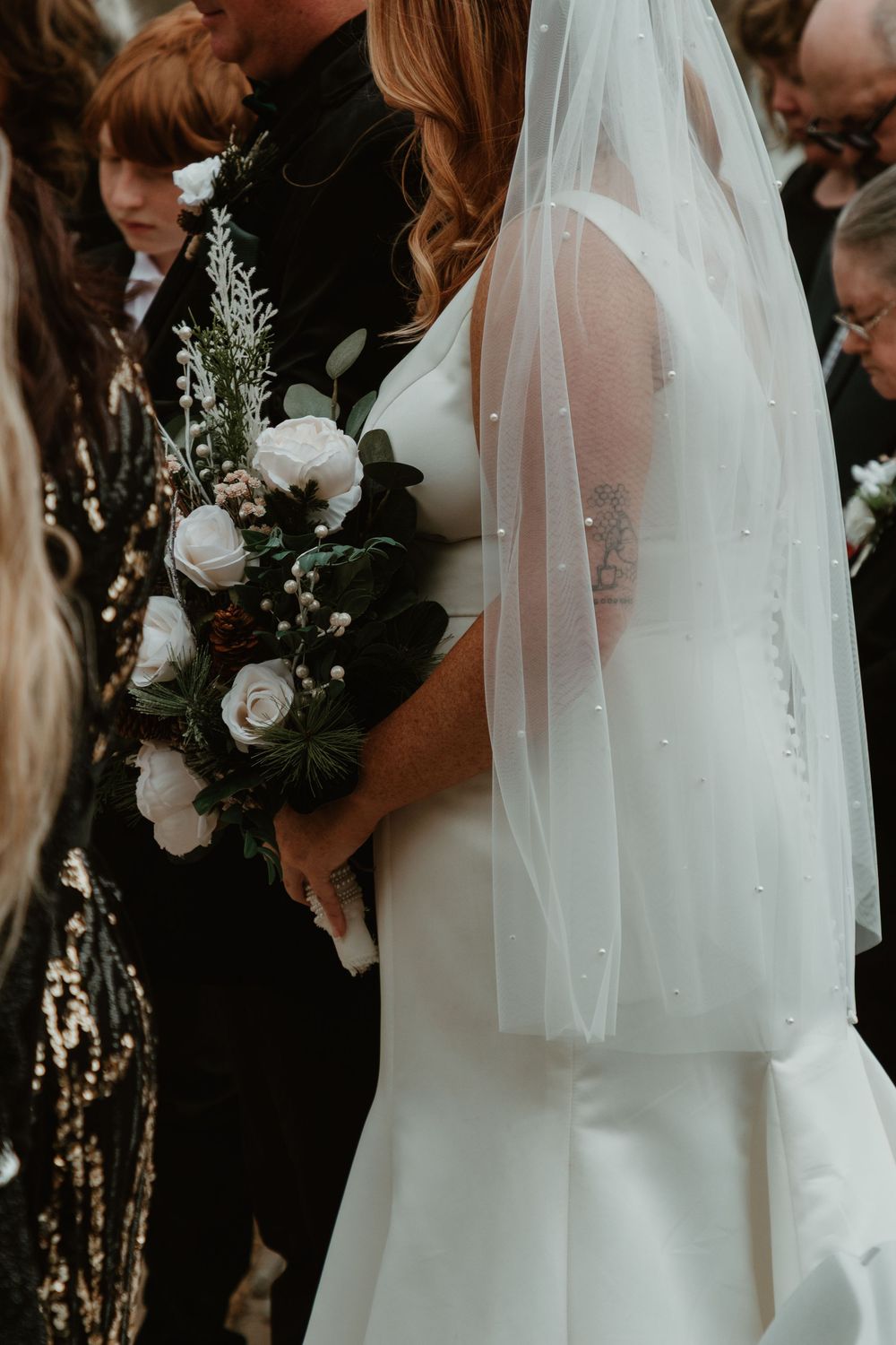 Close-up of white wedding bouquet with roses and greenery against a flowing white veil and dress.