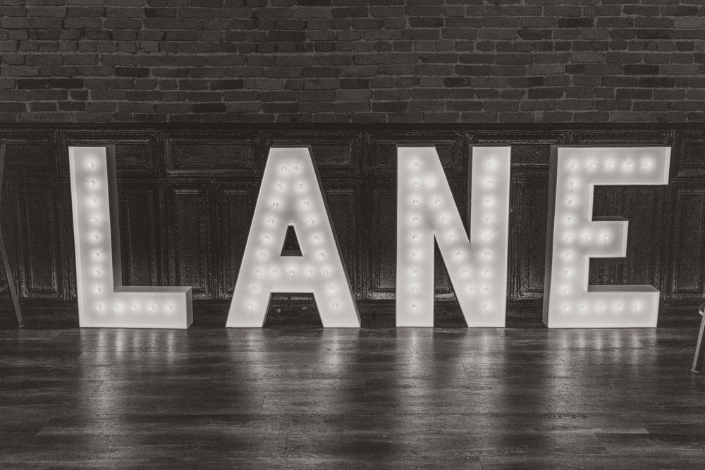 Illuminated white letters spelling out LANE mounted on a dark brick wall in an urban setting.