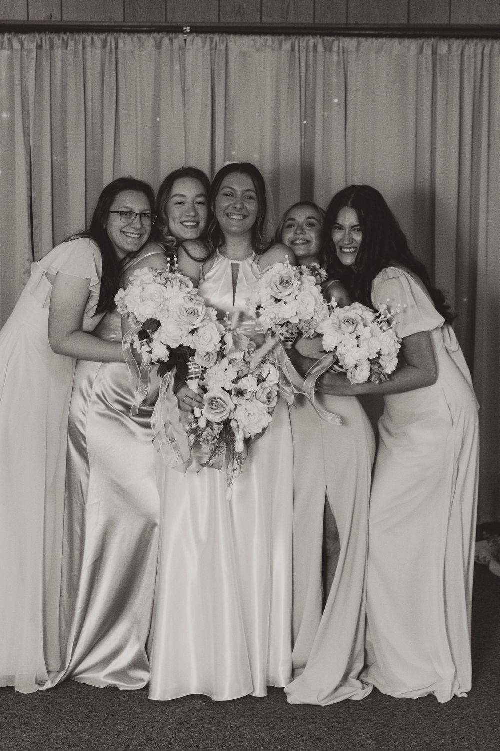 Black and white photo of bridesmaids in white dresses holding floral bouquets while posing together in a line.