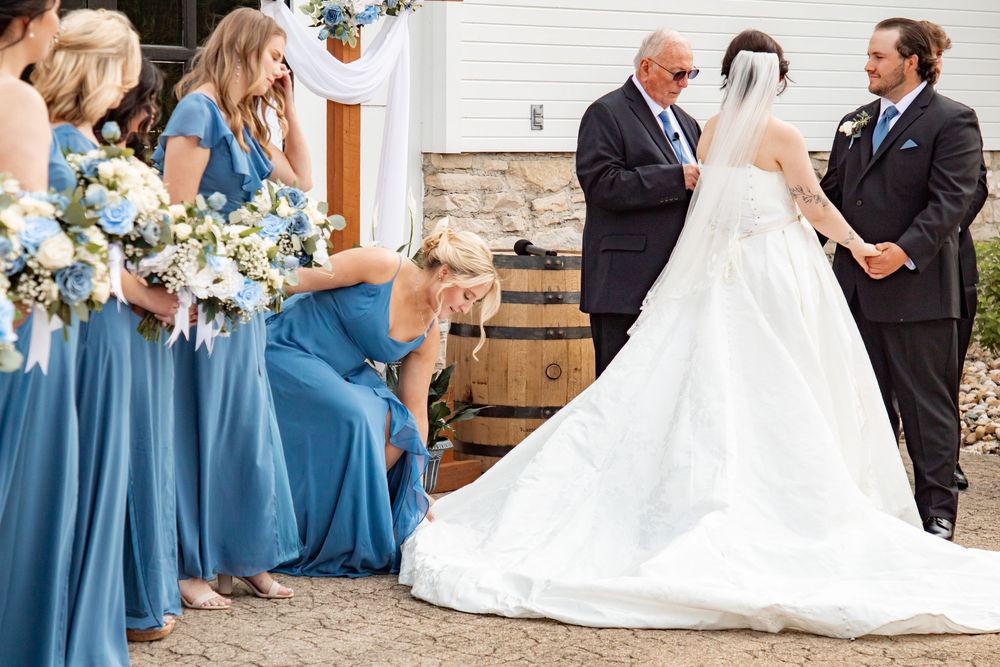 Wedding party members in blue dresses and formal attire gather for celebration photos at a venue.