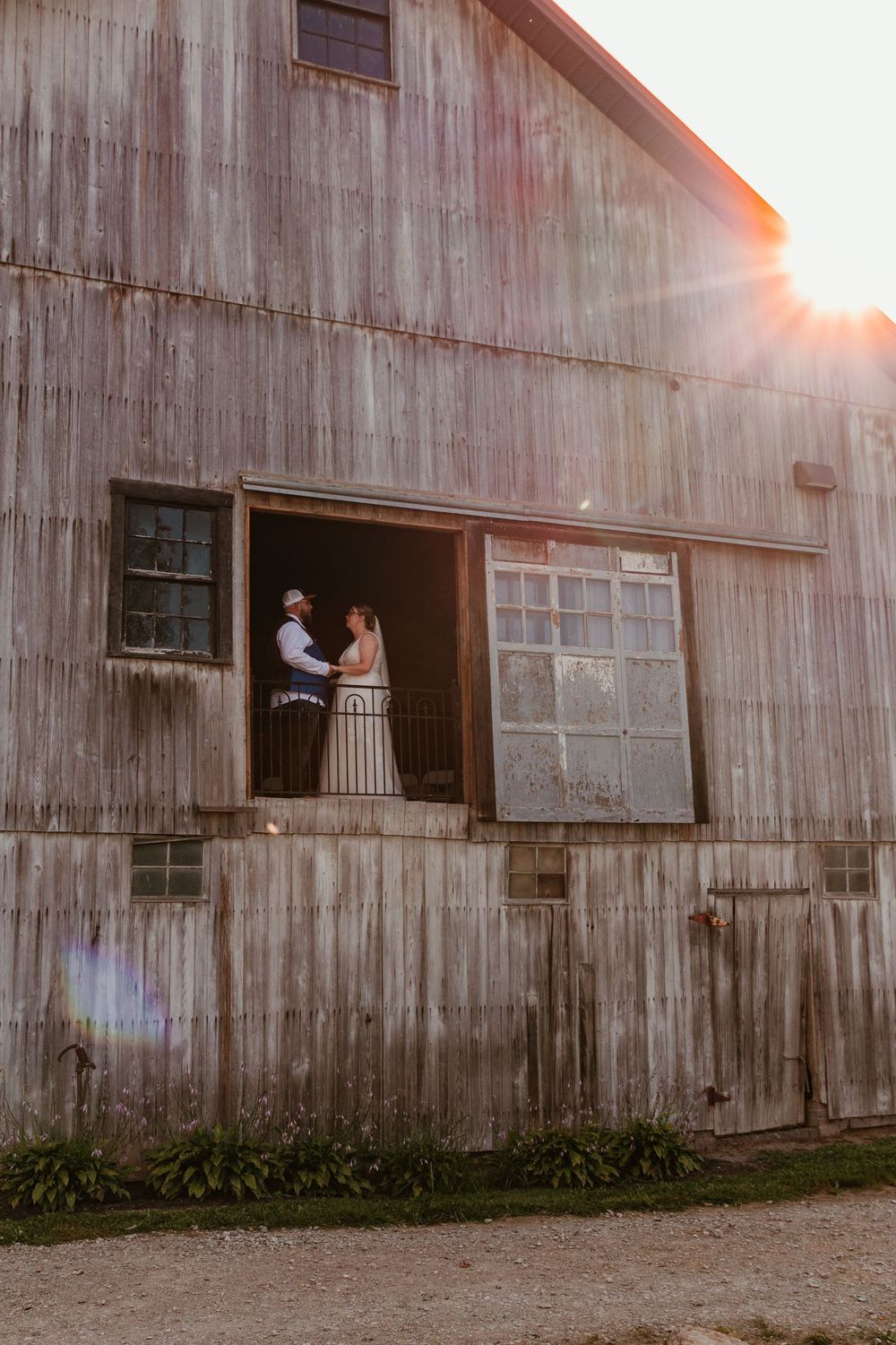 Rustic weathered barn with figures silhouetted in window opening at sunset creating dramatic lighting and atmosphere.