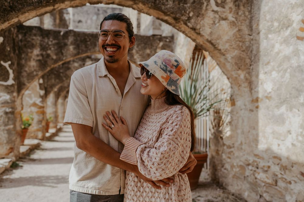 A couple laughs together under stone arches in warm lighting.