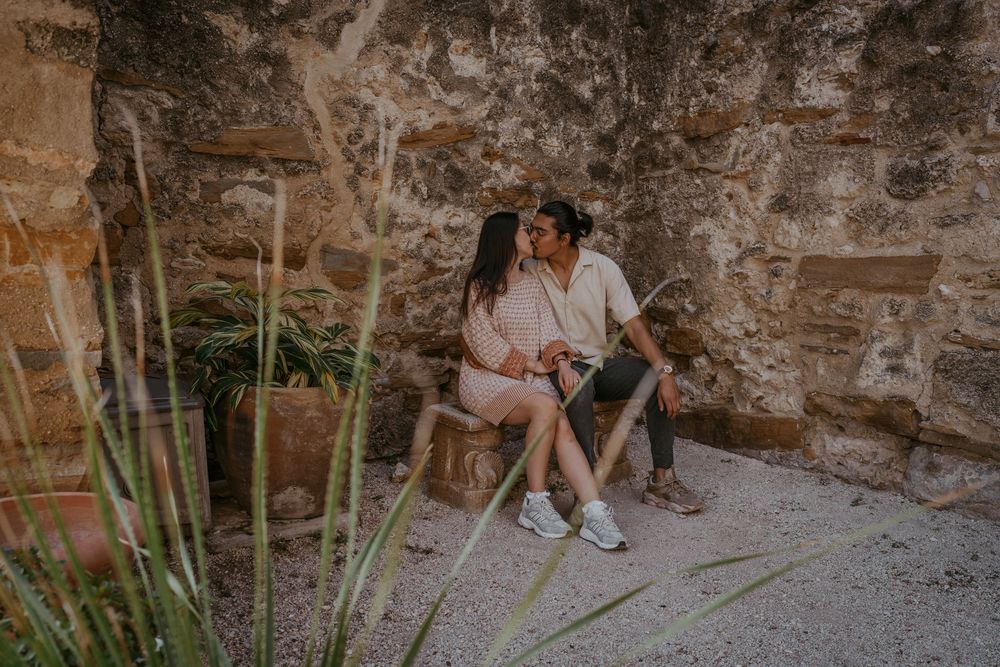A couple sits together on stone steps surrounded by tropical plants.