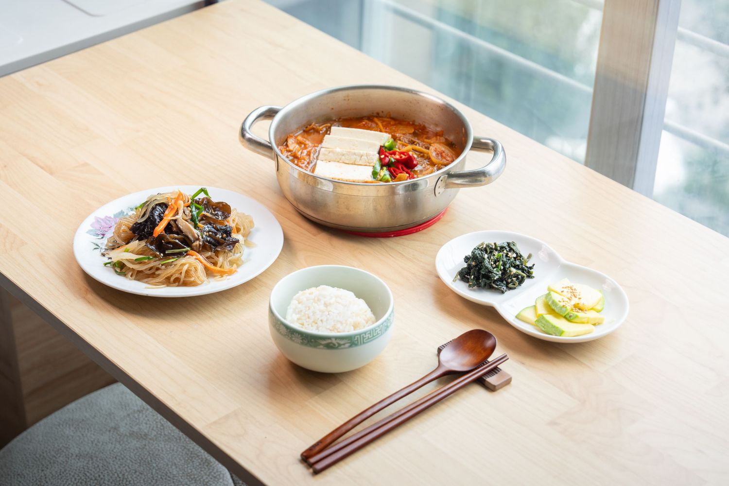 A series of Asian dishes and bowls arranged on a wooden table in natural lighting.