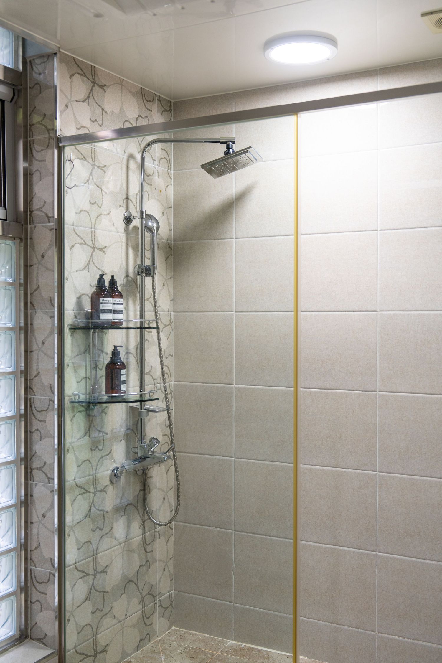 Modern bathroom shower enclosure with glass doors and gray tile walls featuring decorative floral pattern accents.