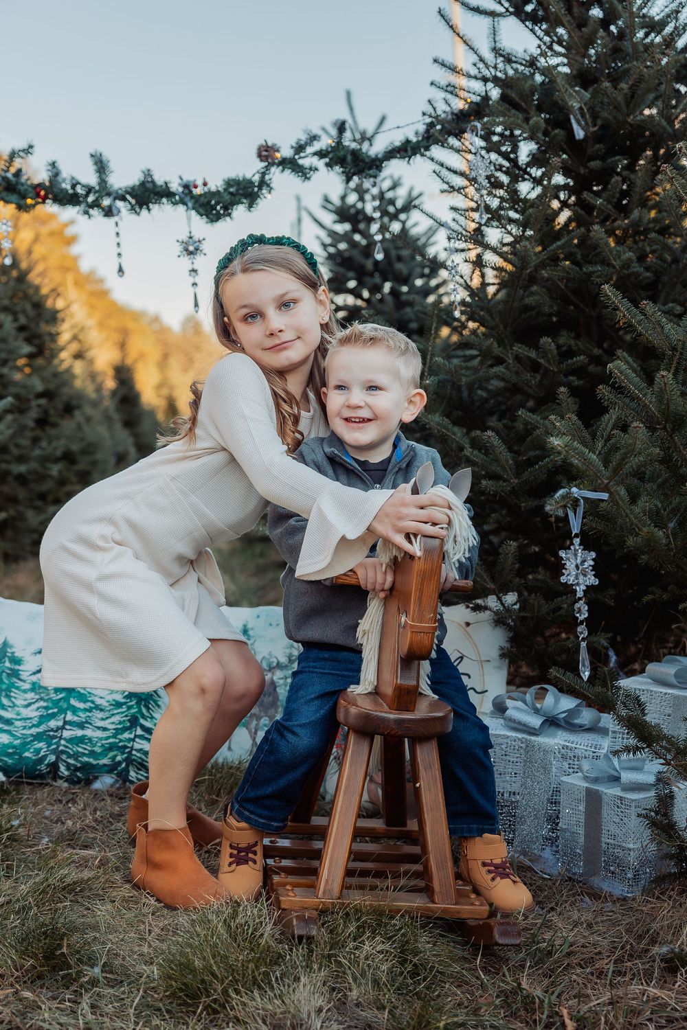 A heartwarming scene at a Christmas tree farm with wooden reindeer decorations among evergreen trees at sunset.