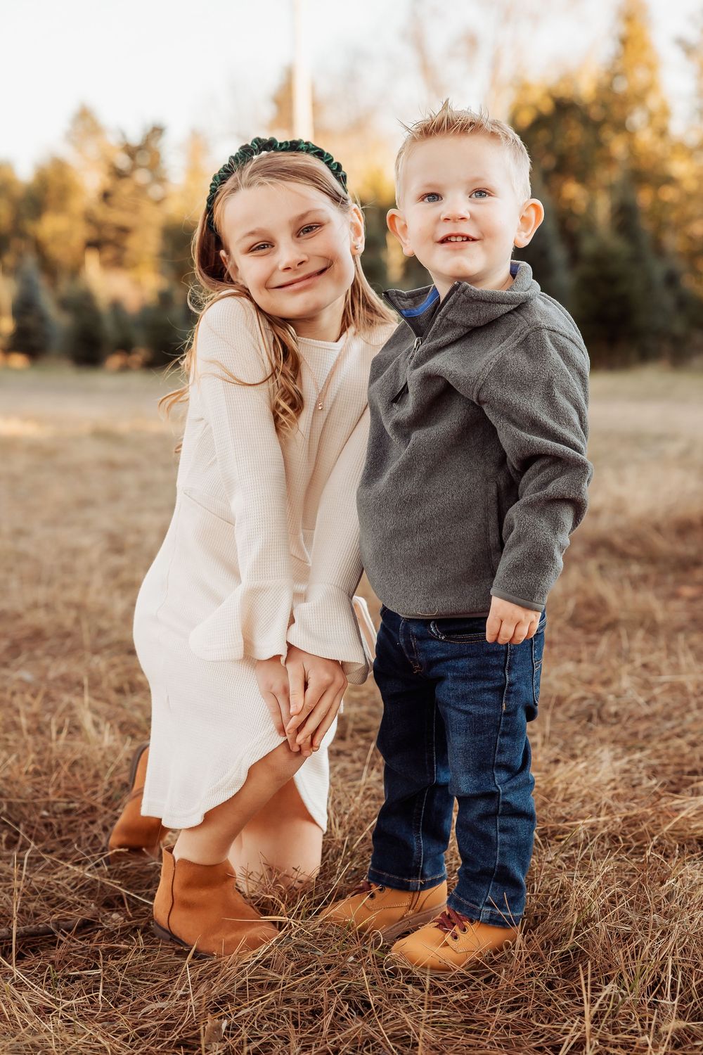 A parent and child in casual fall attire stand together in a golden field at sunset.