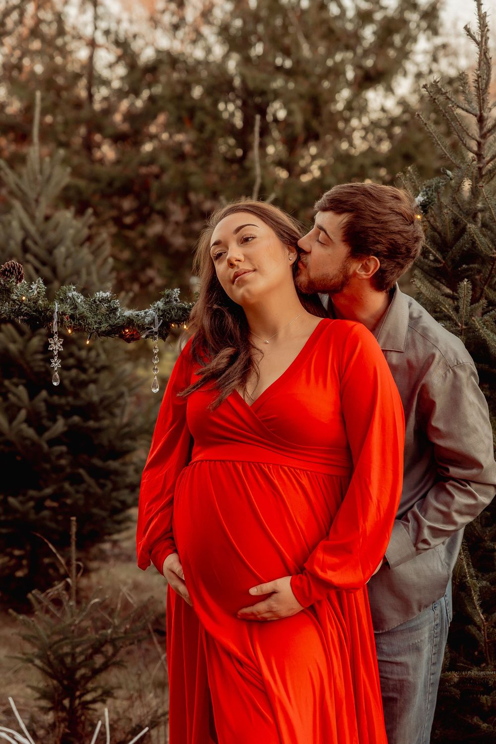 A romantic outdoor maternity photo session featuring a couple embracing, with the person wearing a flowing red dress.