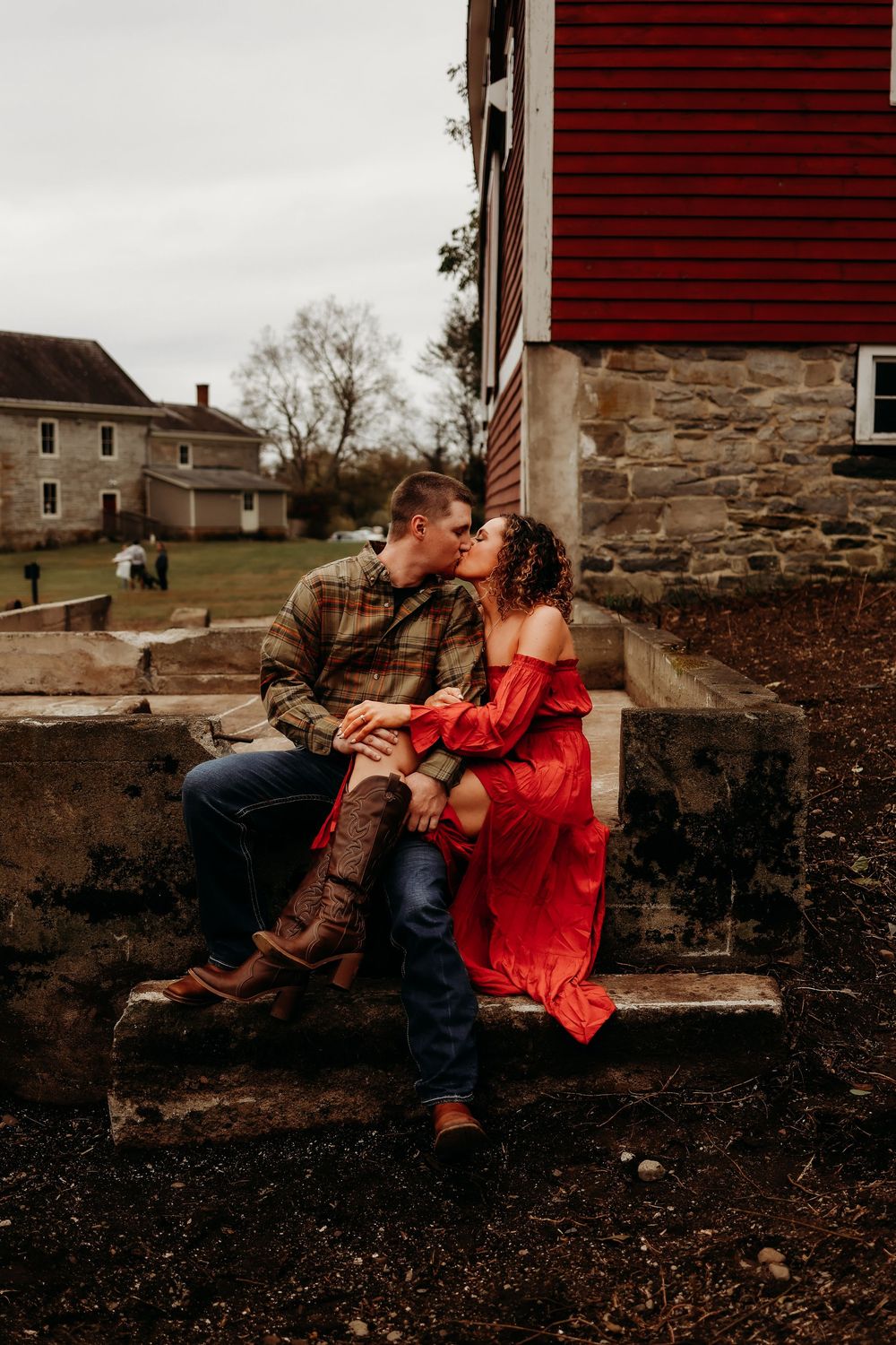 A couple shares an intimate moment together on rustic stone steps with a red barn in the background.