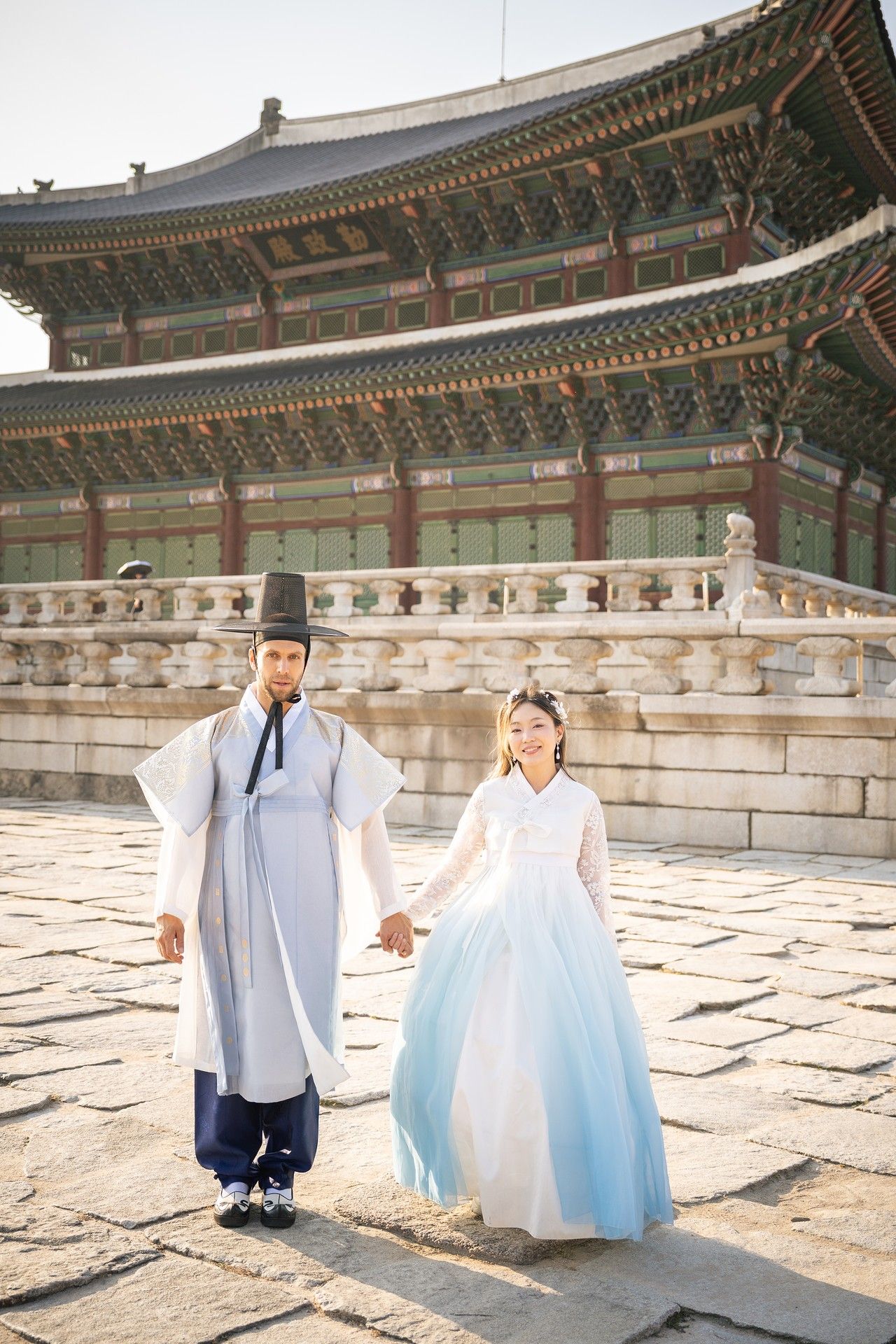 A couple in traditional Korean hanbok outfits walking in a courtyard at Gyeongbokgung Palace.