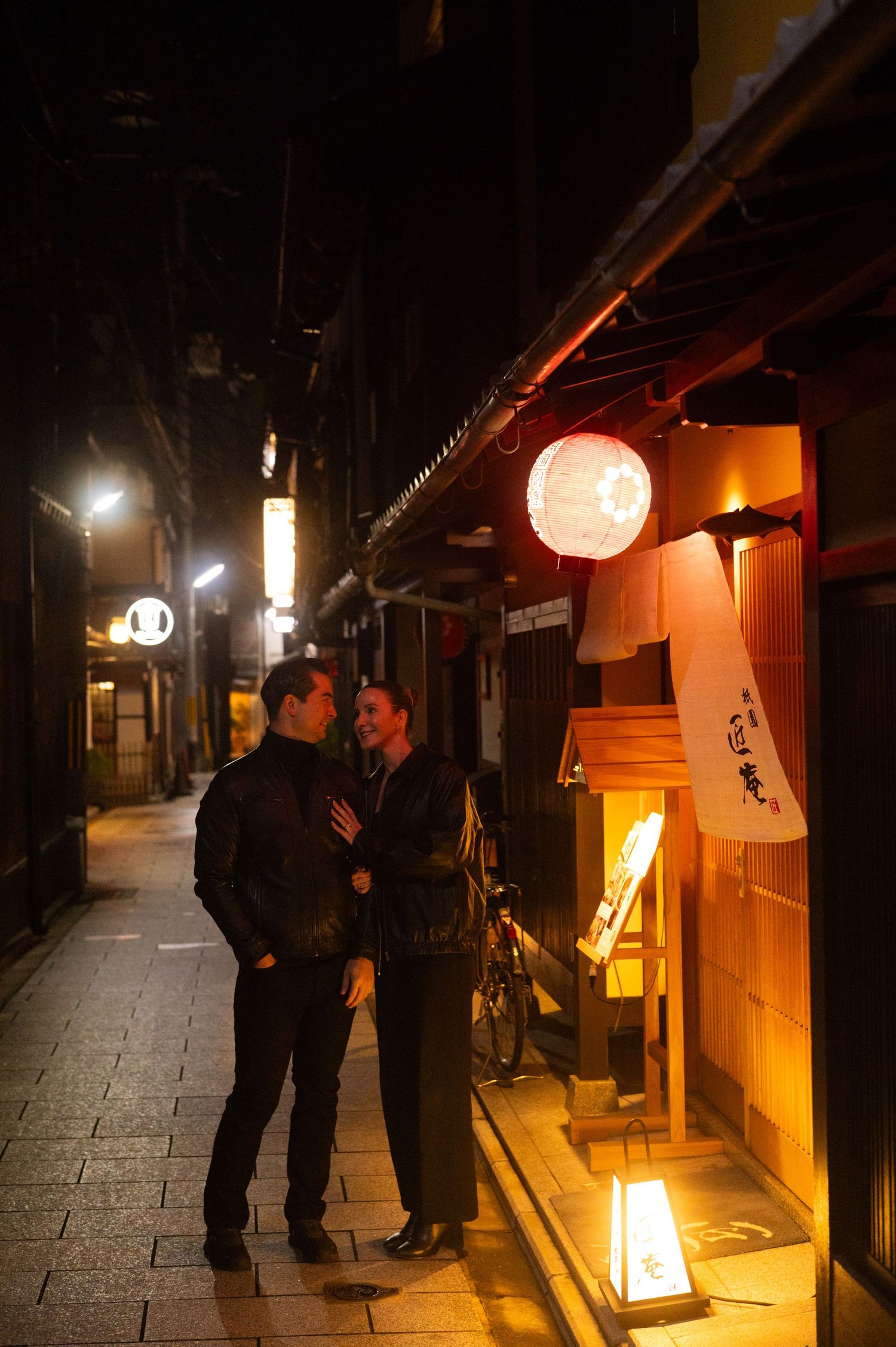 Couple sharing a romantic moment on a lantern-lit Japanese alley at night.