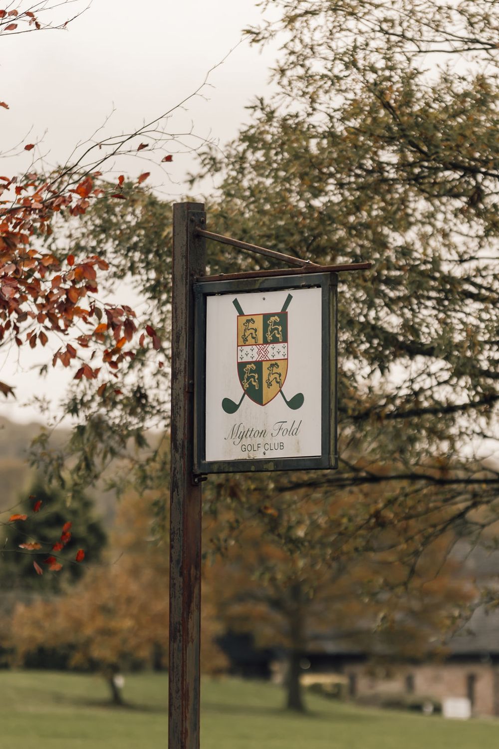 Wooden post sign for Mytton Fold Golf Club against an autumn landscape background.