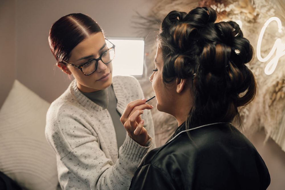 Makeup artist works on bridal beauty preparation in soft lighting.