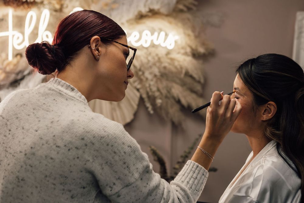 Makeup artist applies finishing touches in a warmly lit bridal suite.