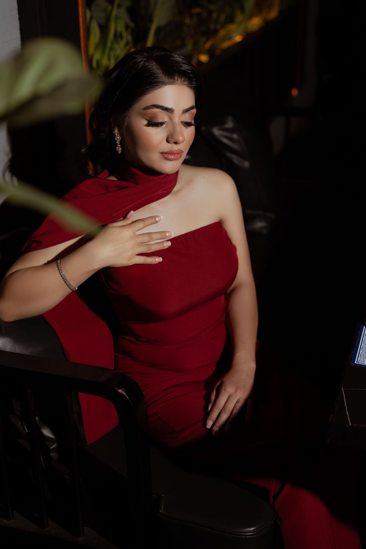 Elegant figure in a form-fitting red evening gown poses gracefully against dark background with dramatic lighting.