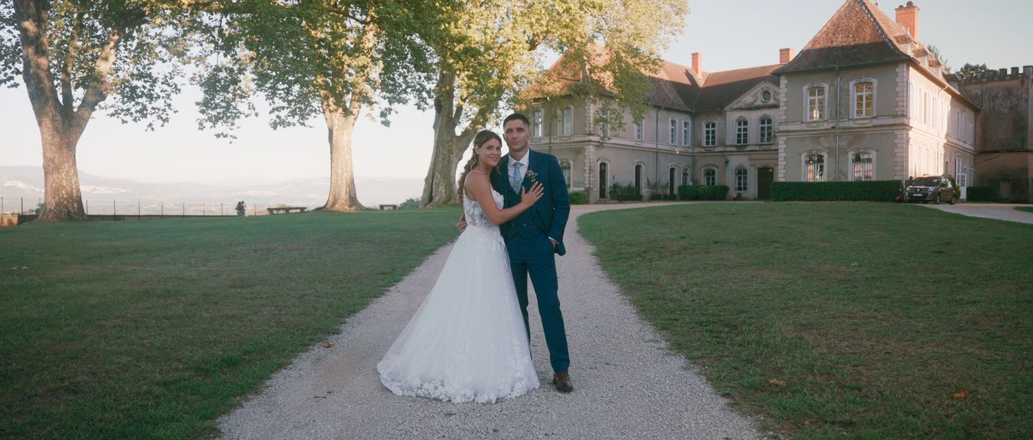 Newlywed couple embraces on scenic castle grounds at sunset during an elegant outdoor wedding celebration.