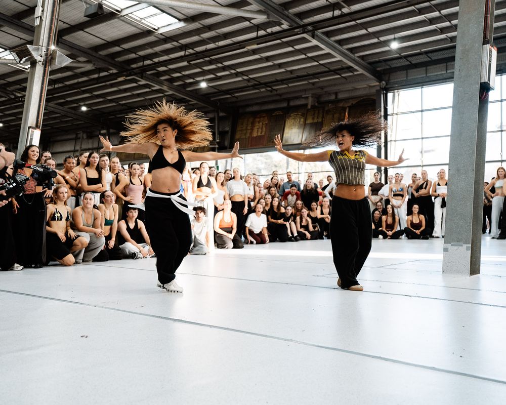 Dance students practicing in a bright studio space with large windows and a mirrored wall.