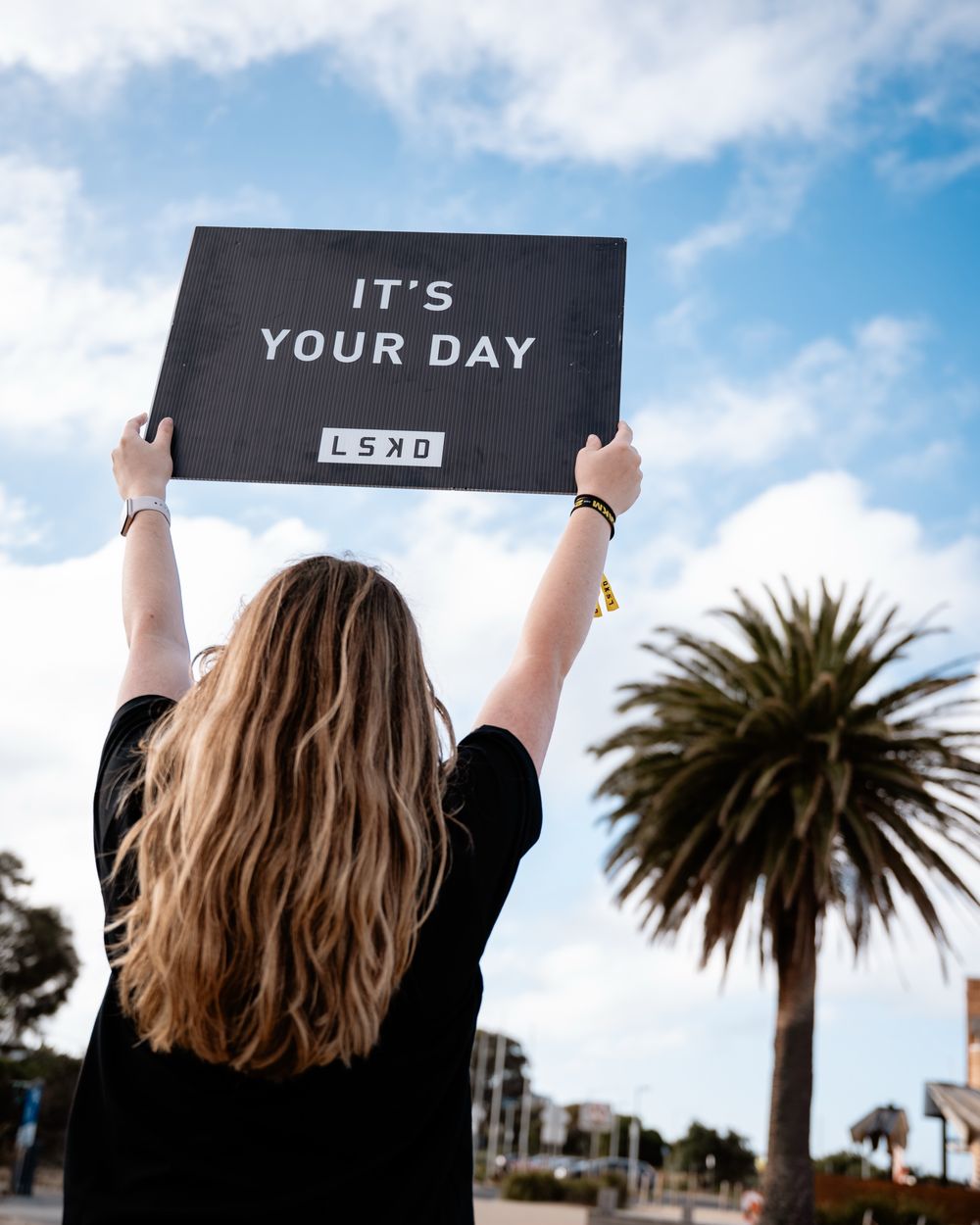 Person holding up a black sign against blue sky with palm trees in a sequence of progressive shots.