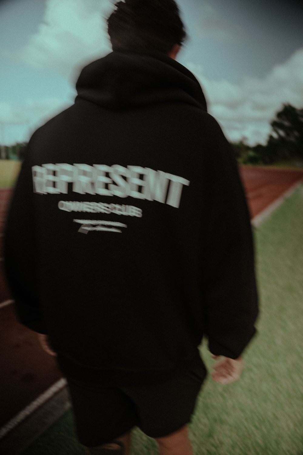 A series of black hoodies with text displayed from different angles on a grassy field background.