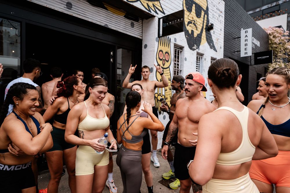 A group of fitness enthusiasts gather together in workout attire at what appears to be a gym or fitness studio.