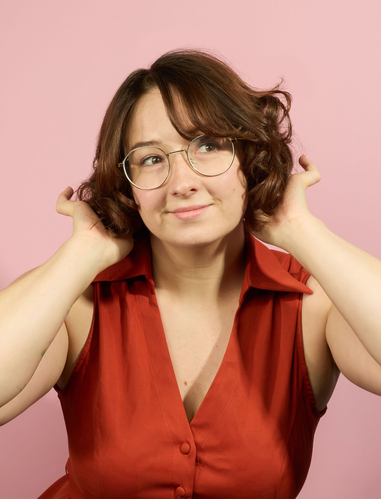A series of four photos showing someone in a red collared top with glasses posing playfully against a pink background.