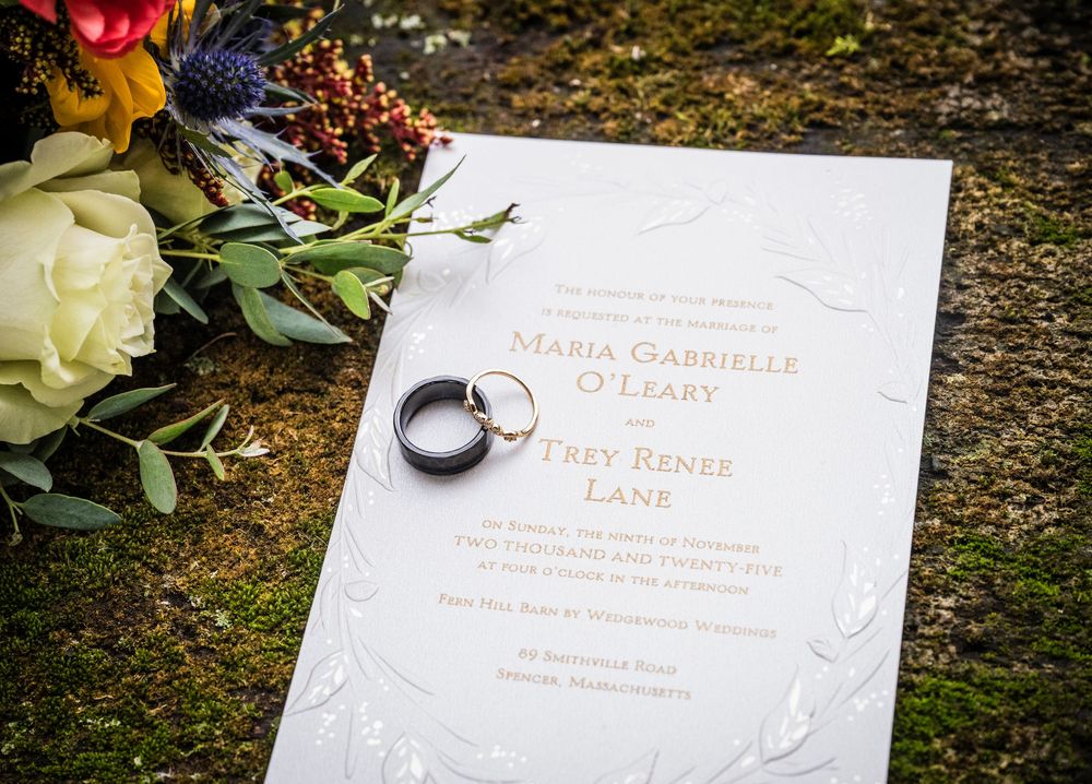 Wedding invitation details with elegant floral decorations and text on white paper against a rustic wooden surface.