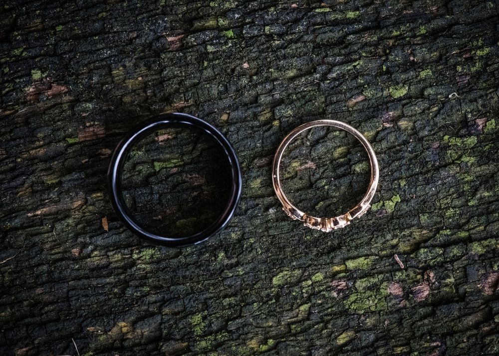 Two wedding rings, one black and one rose gold, placed on a textured mossy stone surface.
