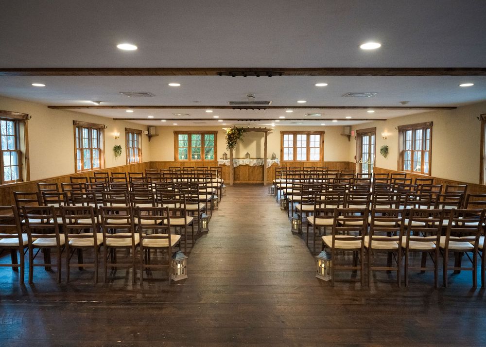 Empty wedding ceremony venue with rows of wooden chairs and recessed lighting in a rustic indoor space.